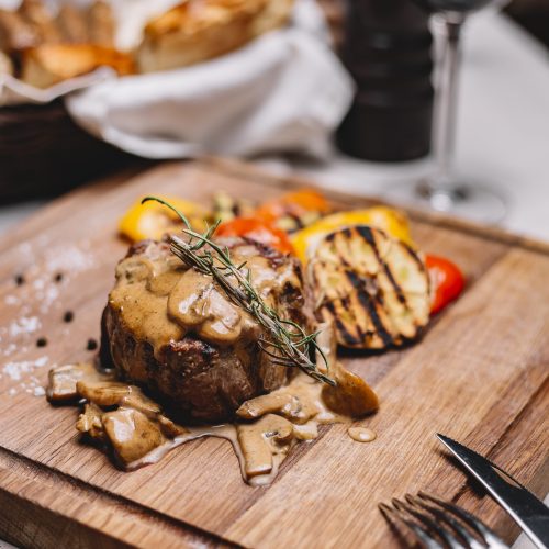 side view of grilled meat medalion with sauce and grilled vegetables on a wooden board